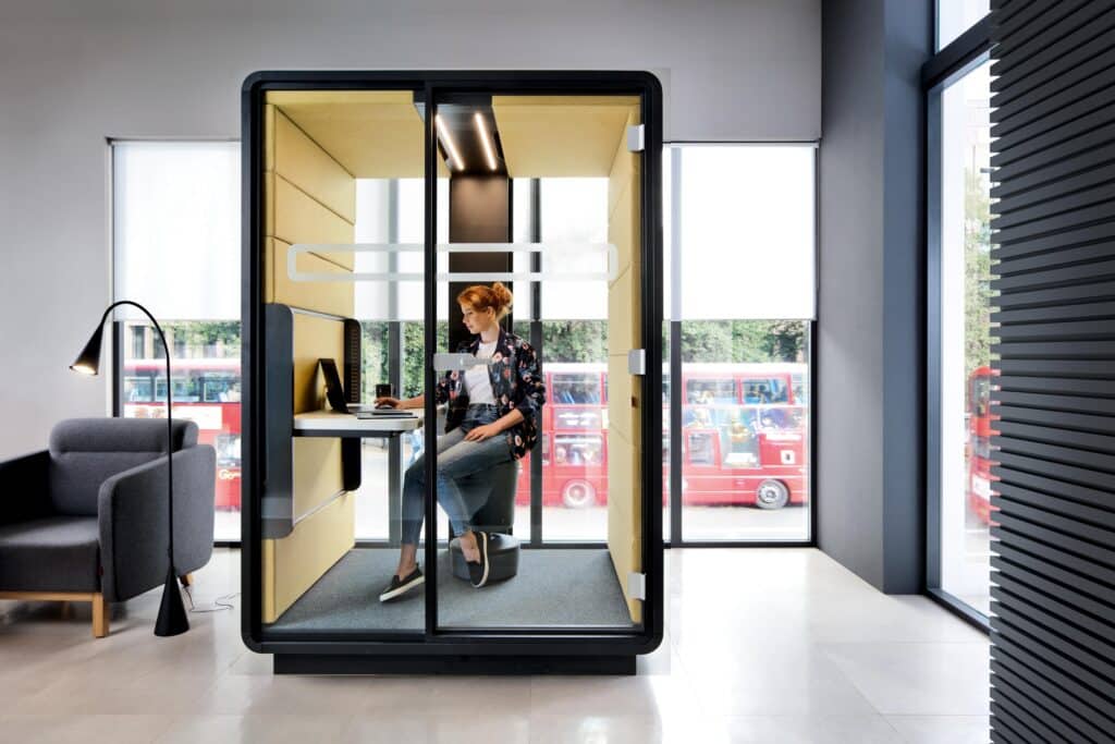 Frau arbeitet in moderner Büro-Kabine mit Fensterblick.