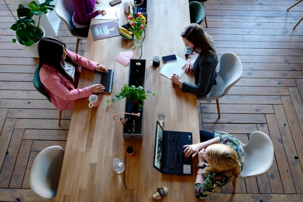 Menschen arbeiten an einem Holztisch mit Laptops.