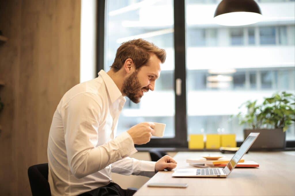 Mann trinkt Kaffee am Laptop im Büro.